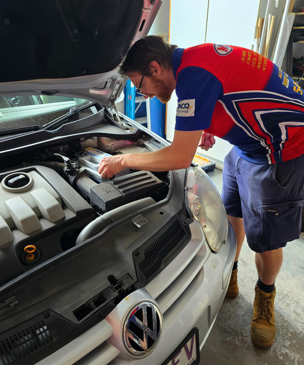 Morayfield Locksmiths technician leaning over a car with the bonnet open, disconnecting the battery to safely rekey the ignition and prevent airbag deployment, providing professional automotive locksmith services in Moreton Bay.