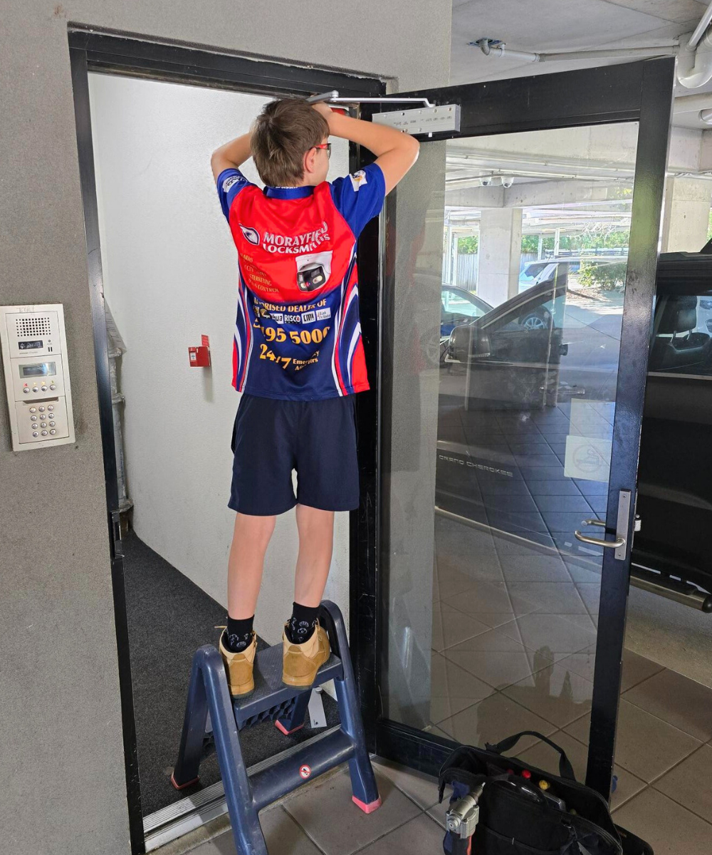Apprentice locksmith from Morayfield Locksmiths adjusting an electronic soft door closer in a commercial doorway in Moreton Bay.